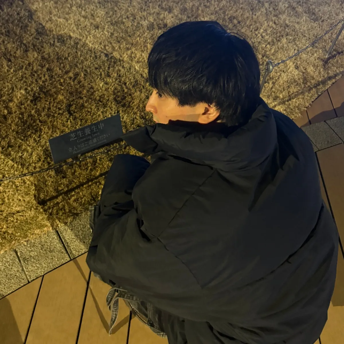夜、芝生のそばにしゃがむ樋口拓実の後ろ姿